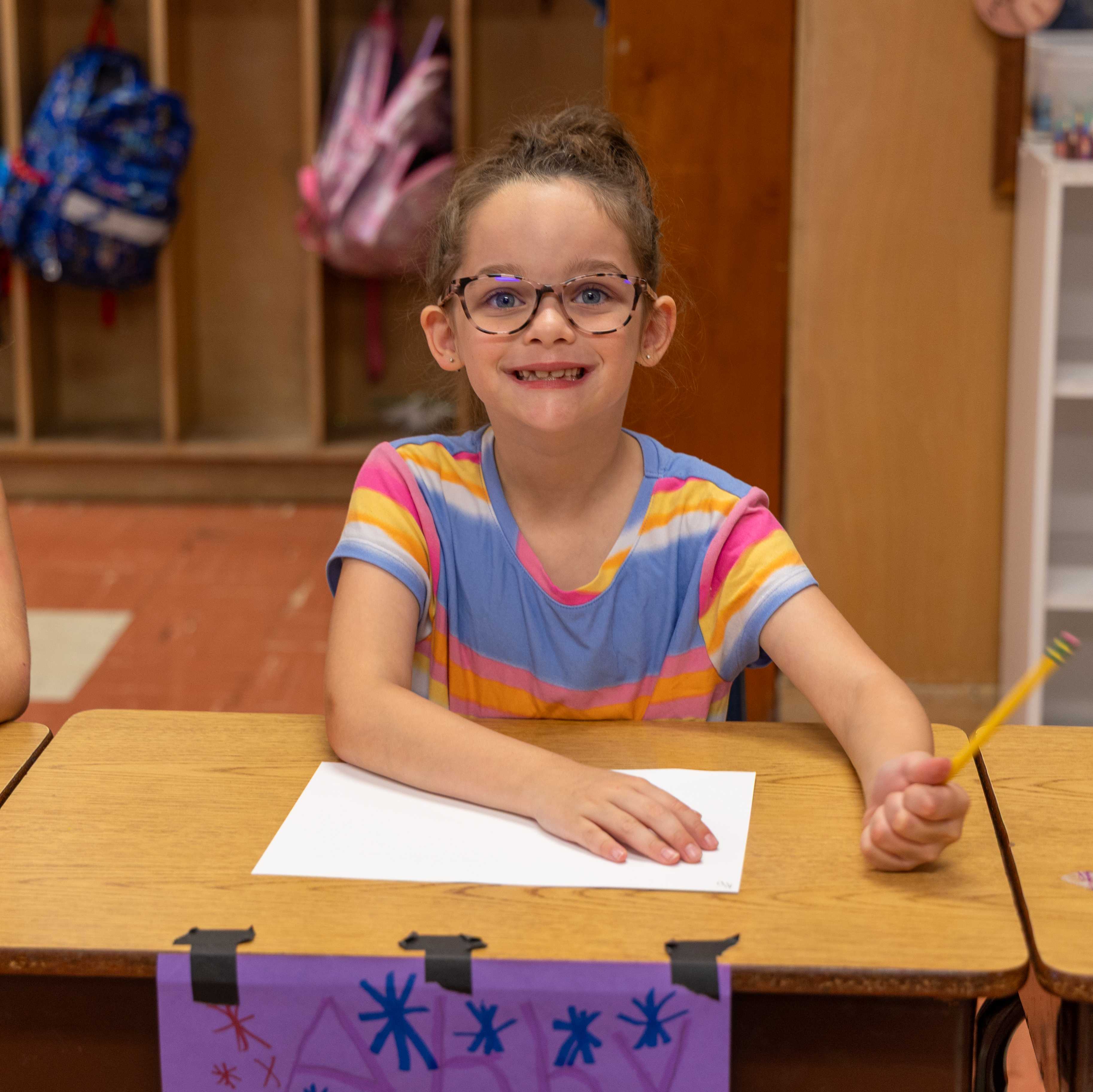 A student smiles at her desk, working on a worksheet